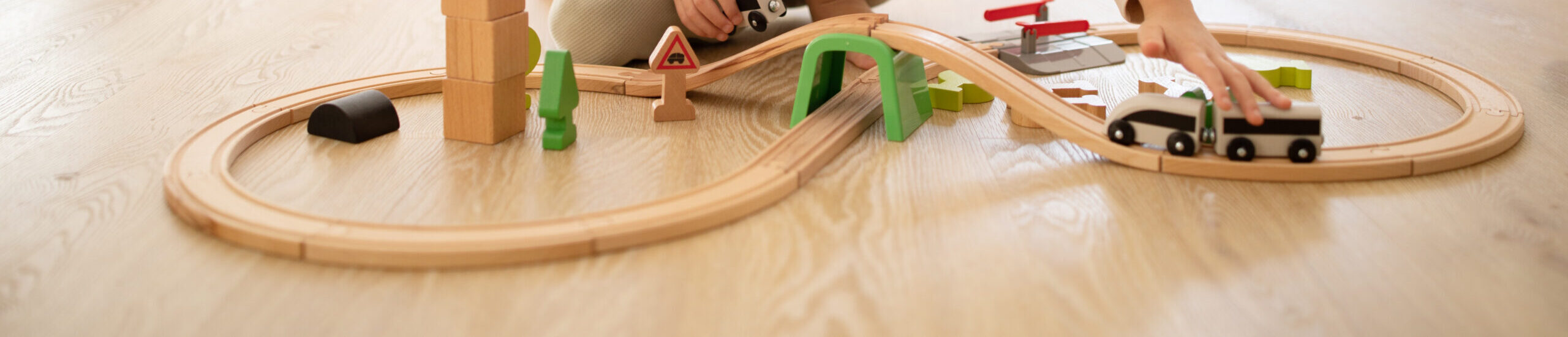 Smiling european small kid in pajamas plays with toys, train, cars and wooden road, sits on floor
