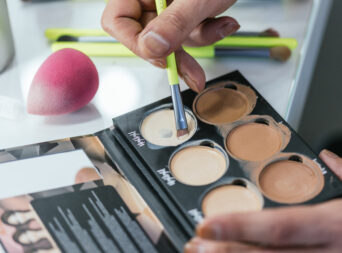 Close-up of a drag queen’s hands applying foundation from a palette